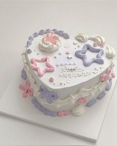 a heart shaped birthday cake on top of a white tablecloth with pink, purple and blue decorations