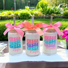 three jars with pink bows are sitting on a table in front of some flowers and grass