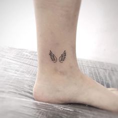 a small ankle tattoo with two wings on the top and bottom of the foot, in black ink