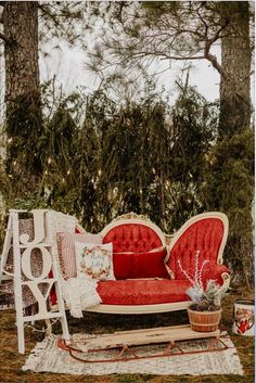 a red couch sitting on top of a grass covered field next to a forest filled with trees