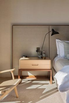 a bedroom with a bed, nightstand and chair next to each other in front of a window