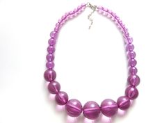 "Gorgeous lucite bead necklace in a lovely purple amethyst color.  All of the beads are completely translucent   The beads are graduated in size from the largest of one inch in diameter at the front to the smaller beads of 1/4\" inch around the back.  Necklace measures 51 centimeters or 20 inches plus a 2.5 inch extender chain. Lobster claw clasp, silvertone fittings.  Excellent condition." Purple Beaded Necklace With Large Beads For Party, Purple Necklaces With Polished Beads For Party, Purple Polished Beads For Party, Polished Purple Beads For Party, Polished Purple Party Beads, Purple Faceted Beads Round Beaded Necklace, Purple Beaded Necklace With Faceted Beads, Purple Round Beaded Necklace With Faceted Beads, Back Necklace