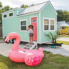 a woman standing next to a pink flamingo in front of a tiny blue house