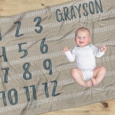 a baby laying on top of a wooden floor next to a blanket that says grayson