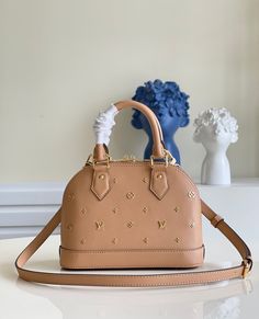 Made from calfskin leather with a glamorous metallic Monogram pattern, this adorably sized Alma BB handbag is instantly recognizable. The iconic shape and signature House details – padlock, rolled leather handles, and key bell – make this small bag a classic. A detachable strap enables shoulder and cross-body wear. Detailed Features 23.5 x 17.5 x 11.5 cm (Length x height x width ) Camel Brown Calfskin leather Monogram Jacquard textile lining Gold-color hardware Double-zip lockable with padlock I Alma Bb, House Details, Lv Bags, Monogram Pattern, Handbags Online, Coach Bag, Vuitton Bag, Leather Handles, Small Bag