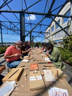 several people sitting at a long table working on crafts