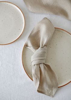 two plates with napkins tied around them on a white table cloth covered place setting