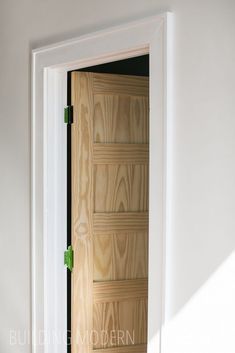 an open door in a white room with wood paneling on the side and green handles