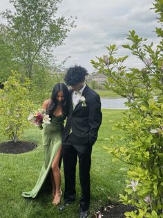 a man and woman dressed in formal wear standing next to each other on the grass