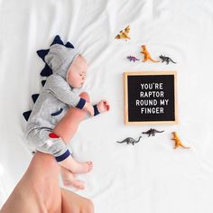 a baby laying on top of a bed next to toy dinosaurs and a sign that says, you're raptor round my finger