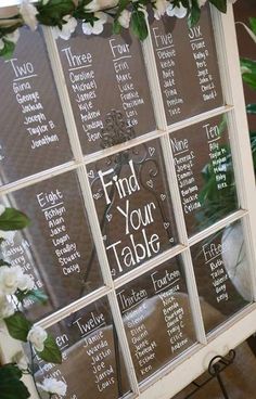 an old window is decorated with white flowers and greenery for a wedding seating plan