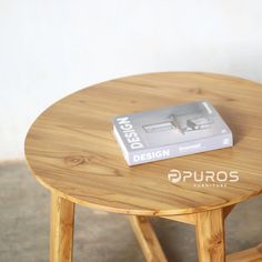 a small wooden table with a book on it's top sitting next to a white wall