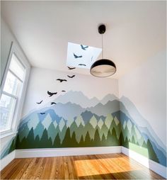 an empty room with birds flying over the mountains painted on the wall and wood flooring