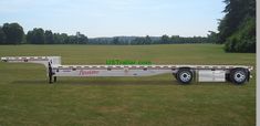 a flatbed trailer is parked in the middle of a grassy field with trees behind it