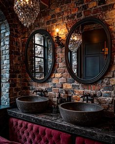 two sinks in front of a brick wall with round mirrors above them and a chandelier hanging from the ceiling