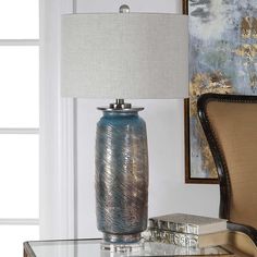 a blue vase sitting on top of a glass table next to a lamp with a white shade