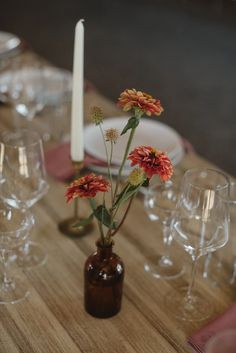 an arrangement of flowers in a brown vase on a table with wine glasses and candles