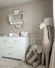 an elephant and giraffe stuffed animals in a baby's room with white furniture