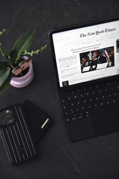 an open laptop computer sitting on top of a table next to a cell phone and plant