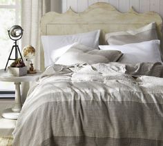 a bed with white sheets and pillows in a bedroom next to a table, lamp and window