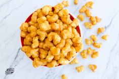 a red bowl filled with popcorn sitting on top of a white counter next to a pile of cashews