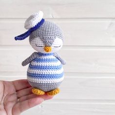 a small crocheted penguin in a blue and white striped dress is held up by someone's hand