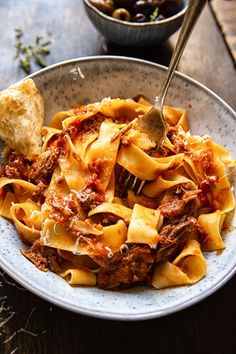 a bowl filled with pasta and meat on top of a wooden table next to bread