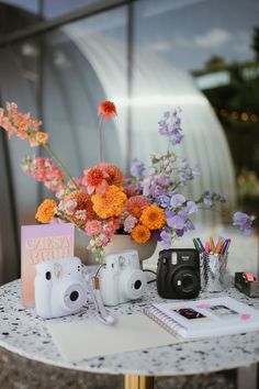 a table topped with flowers and cameras next to a notebook on top of a table