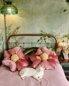 a white cat laying on top of a bed with pink sheets and pillows next to a lamp