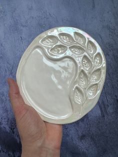 a hand holding a white plate with a tree design on the front and bottom,