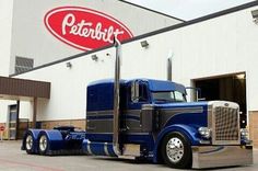 a large blue semi truck parked in front of a building with a logo on it