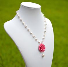 a white mannequin with a pink rose and pearls necklace on it's neck