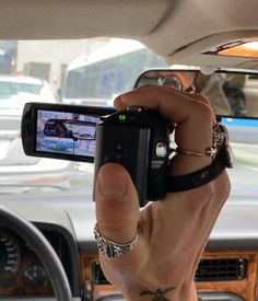 a man holding up his cell phone to take a photo in the car with other cars behind him