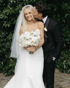 a bride and groom kissing each other in front of some greenery at their wedding