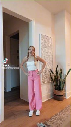 a young woman standing in front of a door wearing pink pants and white tank top