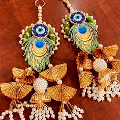 the earrings are decorated with pearls and peacocks in gold, green and blue colors