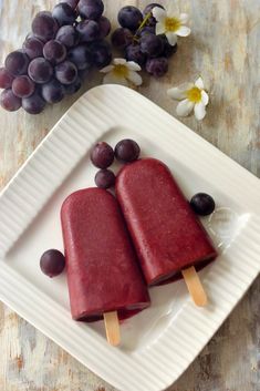 two popsicles on a plate with grapes and flowers