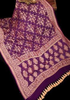 Indulge in a captivating journey that takes you from Banaras, Uttar Pradesh to Kutch, Gujarat with this exquisite saree. Meticulously crafted using the traditional Bandhej technique, it features Shikaargah motifs, beautifully adorned with a jaal pattern. The saree's body boasts of stunning zari elephant, peacock, parrot, and camel motifs alongside intricate floral vines. The border is embellished with elephant and peacock motifs, lending an air of luxury to the ensemble. The resist-dyed dots on Kutch Gujarat, Peacock Motifs, Saree Blouses, Rich Purple, Georgette Saree, Purple Silk, Georgette Fabric, Floral Vine, Uttar Pradesh