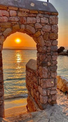 the sun is setting behind an arch in the sand near the water's edge