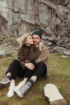 a man and woman sitting next to each other on the ground with rocks in the background