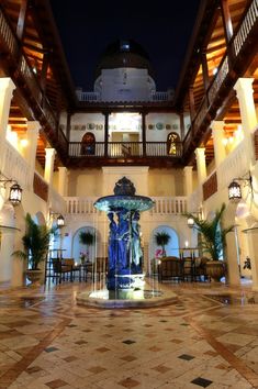 the inside of a large building with a fountain in it's center and lights on