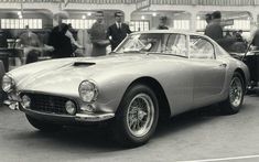 an old black and white photo of a car with people in the background looking at it