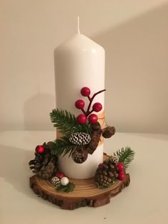 a white candle with pine cones and red berries on it sitting on a wood slice