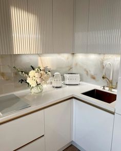 a kitchen with white cabinets and marble counter tops is pictured in this image, there are flowers on the counter