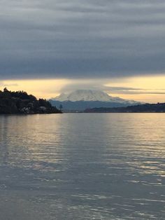 a large body of water with mountains in the background and clouds above it at sunset