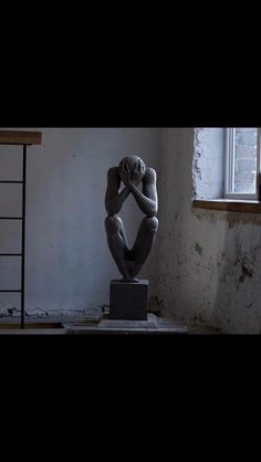 a statue is sitting in the corner of a room with a ladder and window behind it