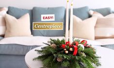 a christmas centerpiece on a table with two candles and evergreen branches in it, next to a couch