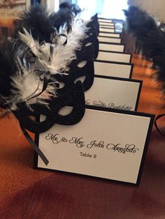 black and white masquerade place cards with feathers on them sitting on a table