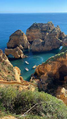 several boats are in the blue water near some rocks and cliffs on a sunny day