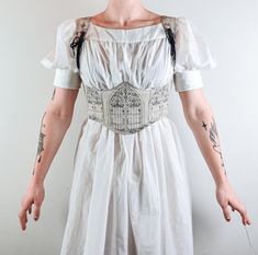 An under-bust corset with a pattern of Gothic cathedral windows against an oatmeal hued background of natural un-dyed linen, inspired by the ethereal elegance of medieval architecture. This piece laces up at the center back through black steel eyelets. The exterior is made from linen (a sustainable textile) while the lining is made from upcycled fabric.This piece is MADE TO ORDER. Be sure to check our Size guide before purchasing.  Made to order garments have a lead time of 4-6 weeks. Note: All Corset Medieval Dress, Gothic Wedding Corset Belt With Boned Bodice, Gothic Wedding Corset Belt With Corset Back, Gothic Underbust Corset Belt For Wedding, Medieval Style Underbust Corset Belt With Boned Bodice, Beige Underbust Corset Belt, Gothic Cathedral Windows, Corset Belt Pattern, Medieval Corset